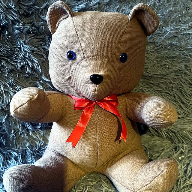 Handmade memory bear in soft tan fabric with a red ribbon